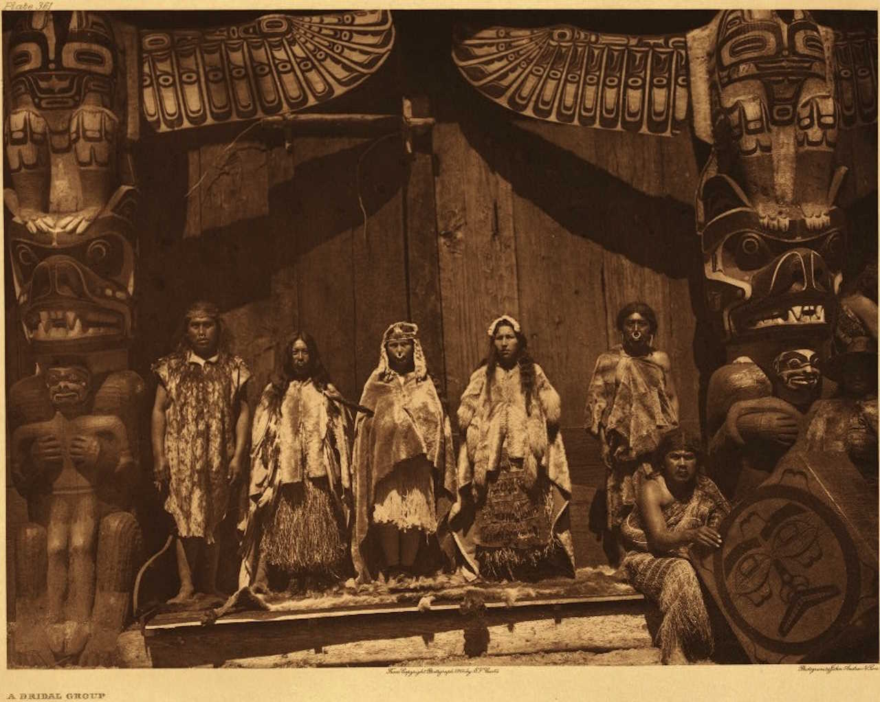 Потлач у народу квакіутль з танцівниками та співаками на весіллі 1914 року, з нареченою у центрі фото. Edward S. Curtis / Wikimedia Commons